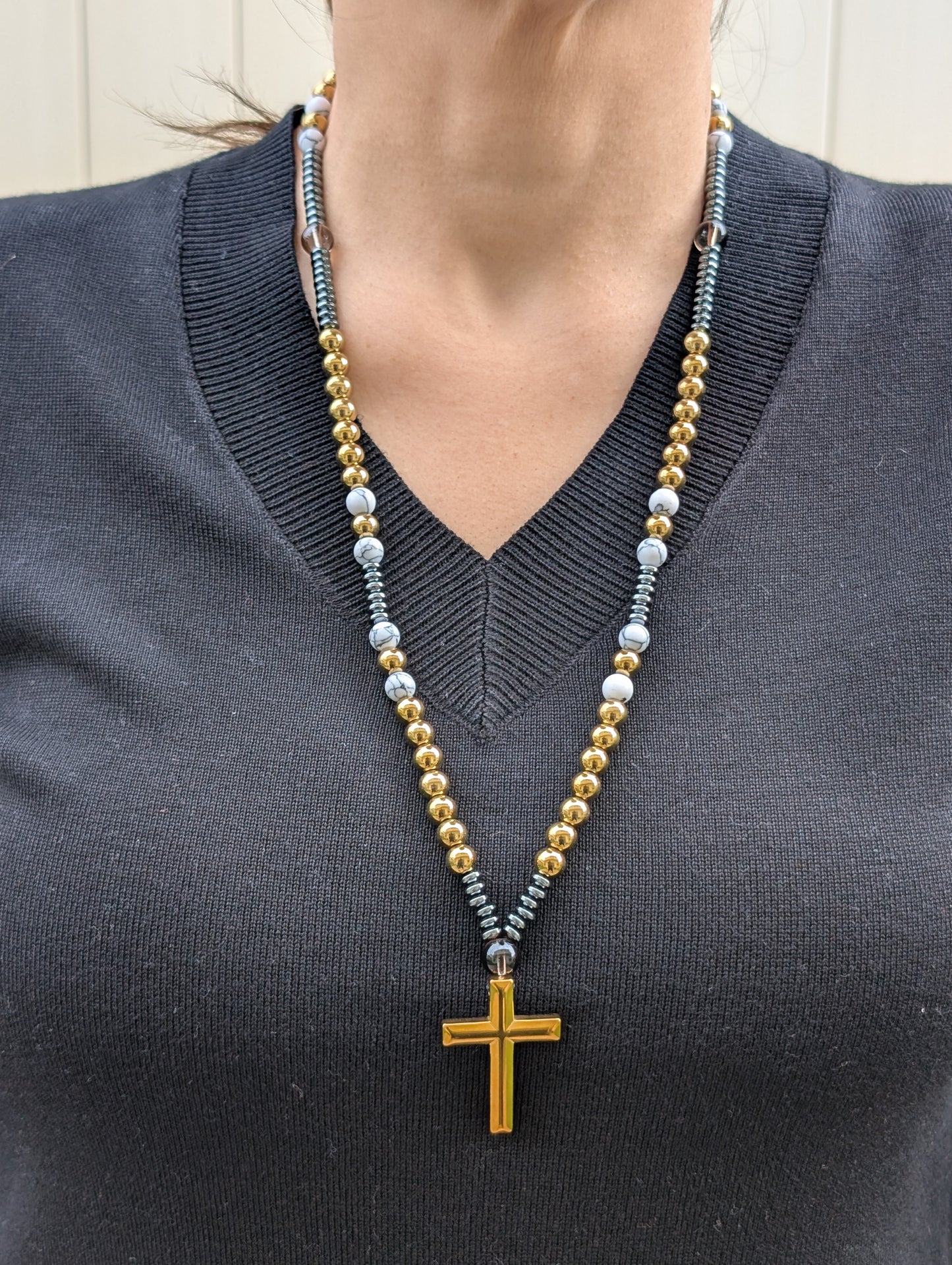 Person wearing a necklace with a cross pendant on a plain background