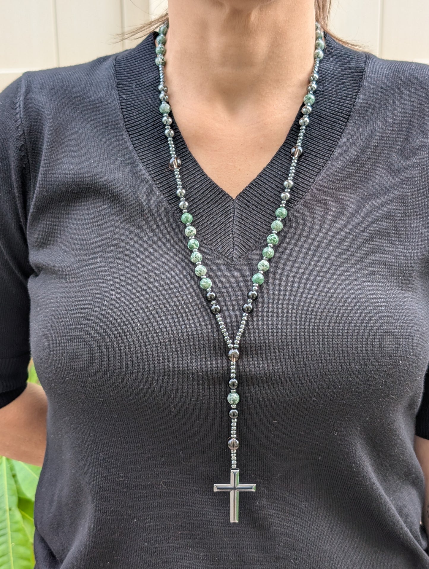 Person wearing a long necklace with a cross pendant on a dark shirt.