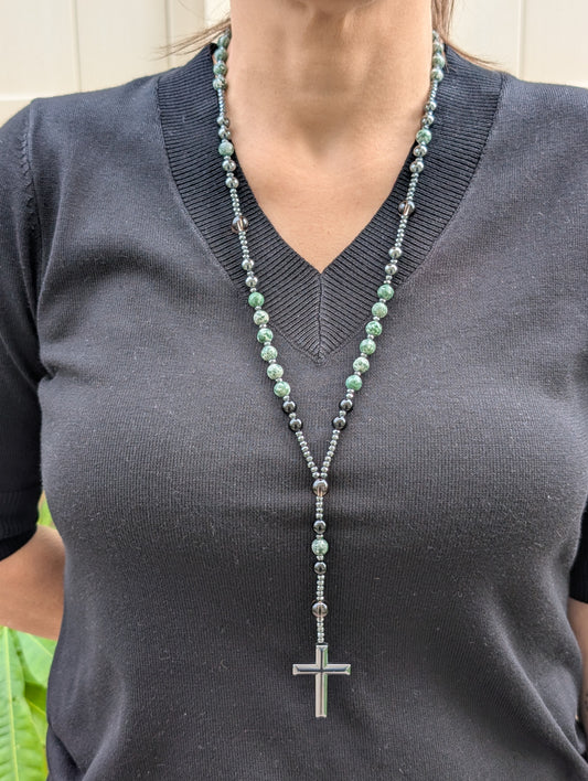 Person wearing a long necklace with a cross pendant on a dark shirt.
