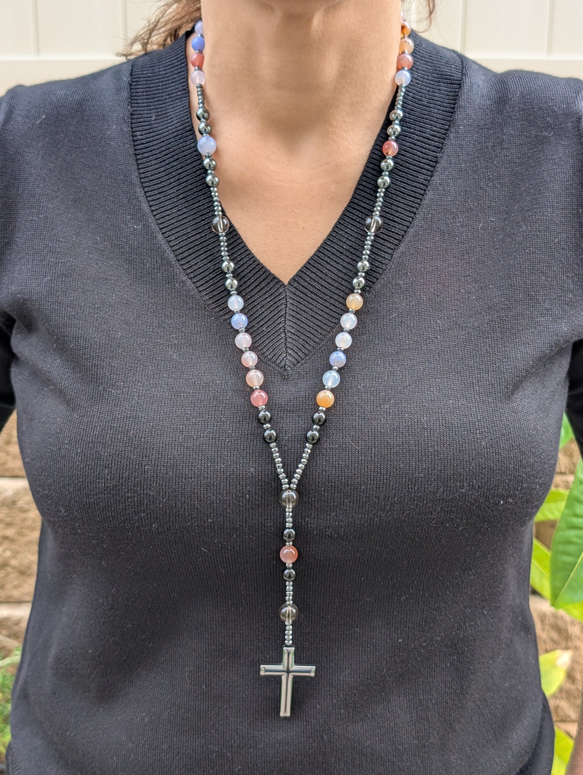 Person wearing a long beaded necklace with a cross pendant on a dark gray shirt.